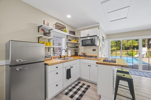 kitchen with tasteful backsplash, open shelves, a sink, wood counters, and appliances with stainless steel finishes