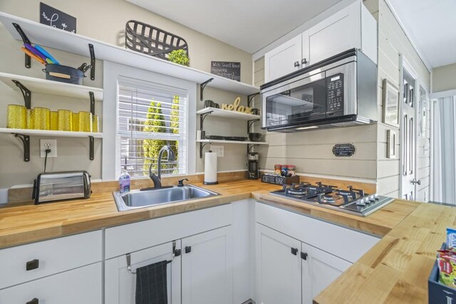 kitchen featuring white cabinetry, open shelves, stainless steel appliances, wooden counters, and a sink