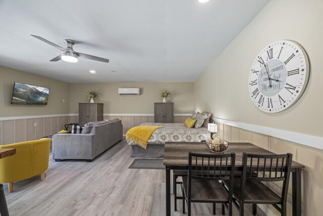dining space featuring a ceiling fan, wood finished floors, a wall mounted air conditioner, and wainscoting