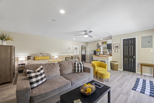 living room with wood walls, recessed lighting, light wood-style floors, a ceiling fan, and electric panel
