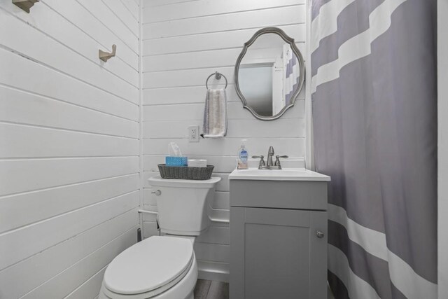 bathroom featuring toilet, vanity, and wood walls