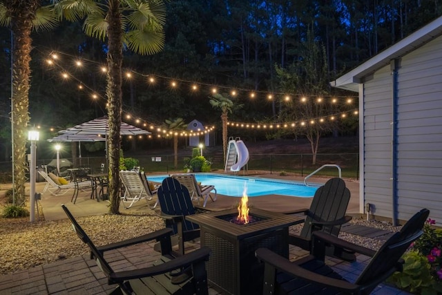 pool at night with an outdoor fire pit, a water slide, and a patio