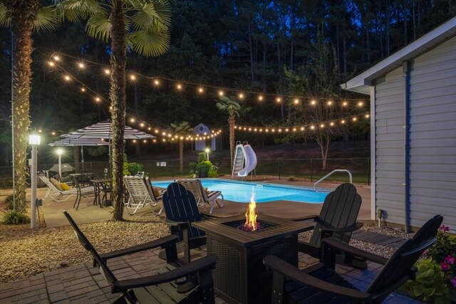 pool at twilight with fence, a water slide, a fenced in pool, a fire pit, and a patio area