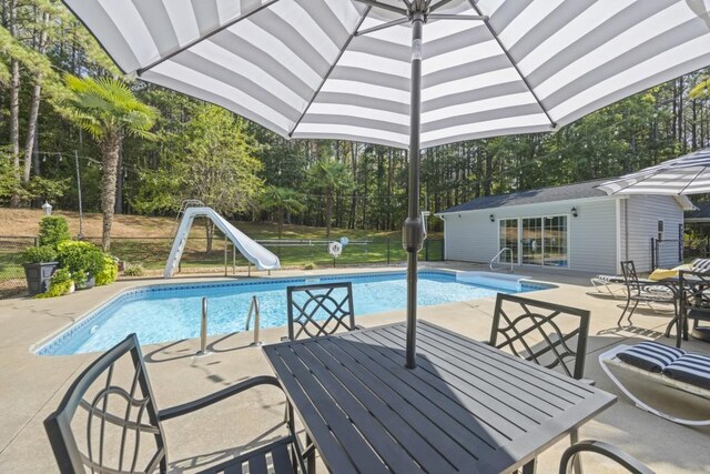 outdoor pool with a water slide, an outbuilding, fence, a patio, and outdoor dining area