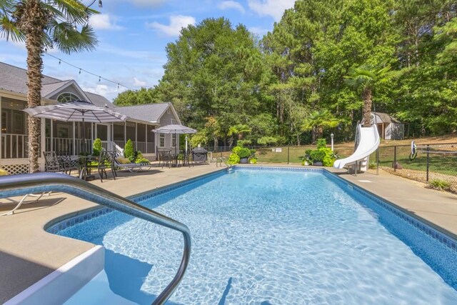 view of swimming pool featuring a fenced in pool, a water slide, fence, a sunroom, and a patio