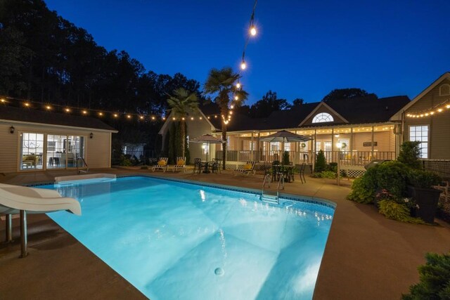 pool at twilight featuring fence, a water slide, a patio area, and a fenced in pool