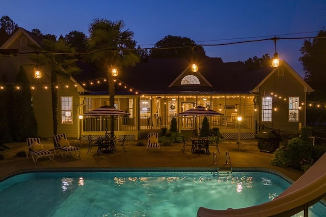 pool at night with a grill, a water slide, and a patio area