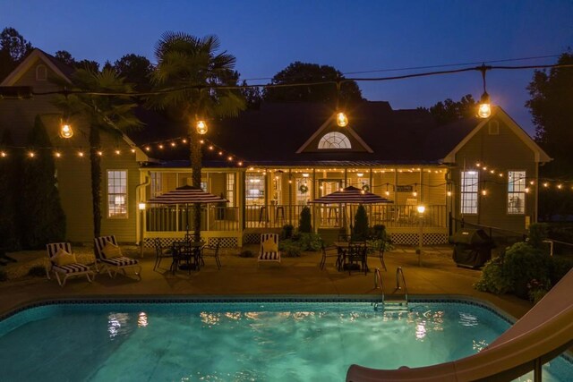pool at night featuring a water slide, an outdoor pool, and a patio area