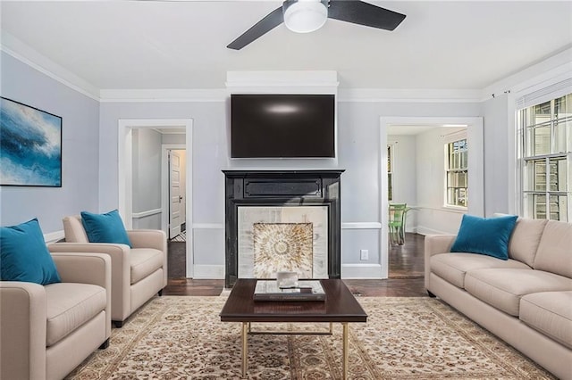 living room featuring crown molding, a fireplace, baseboards, and wood finished floors