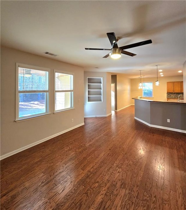 unfurnished living room with ceiling fan, dark hardwood / wood-style flooring, built in features, and sink