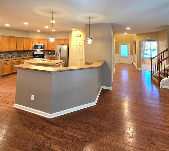 kitchen with appliances with stainless steel finishes, decorative light fixtures, decorative backsplash, sink, and dark hardwood / wood-style floors