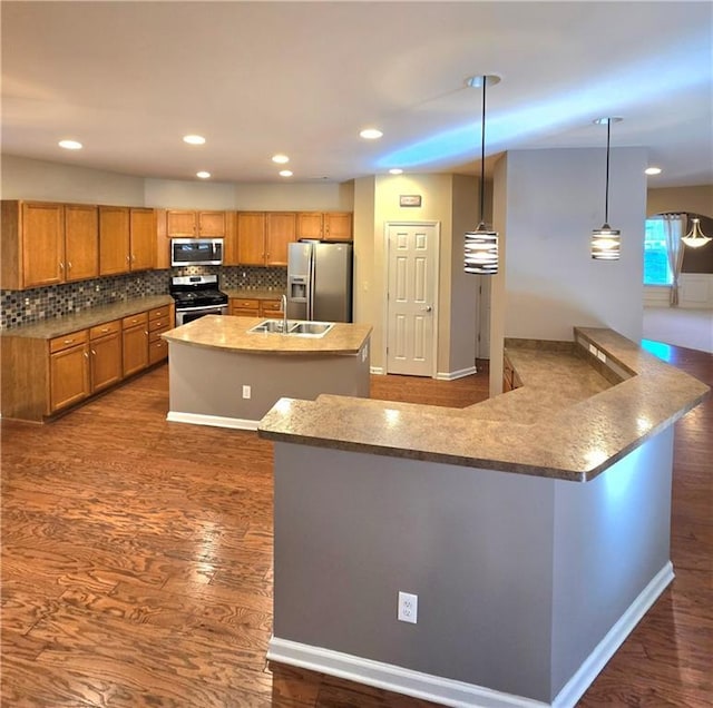 kitchen featuring kitchen peninsula, an island with sink, stainless steel appliances, decorative light fixtures, and dark hardwood / wood-style flooring