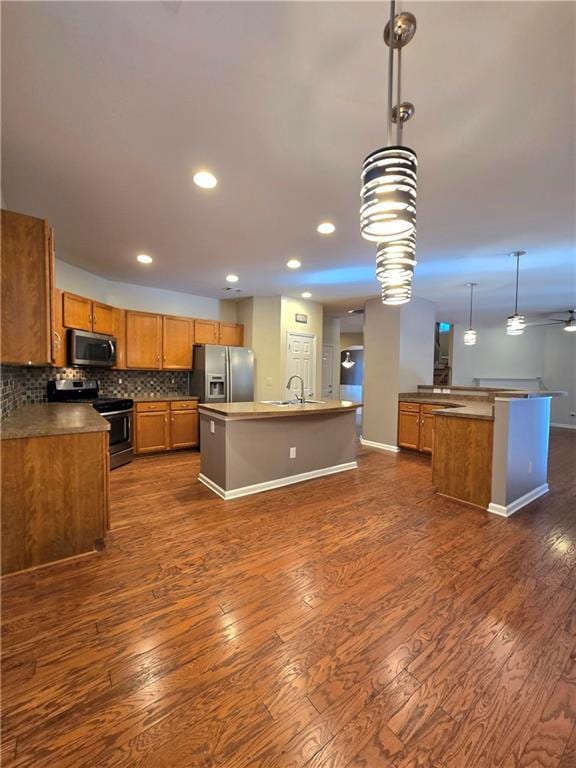 kitchen with a center island with sink, stainless steel appliances, backsplash, pendant lighting, and sink