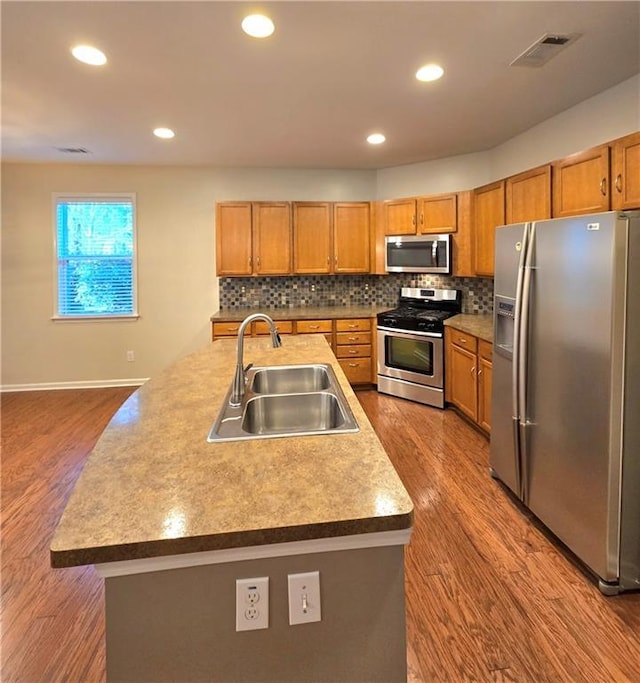 kitchen with backsplash, hardwood / wood-style floors, sink, a kitchen island with sink, and appliances with stainless steel finishes