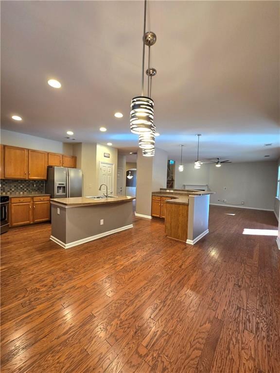 kitchen featuring ceiling fan, tasteful backsplash, pendant lighting, a center island with sink, and stainless steel fridge