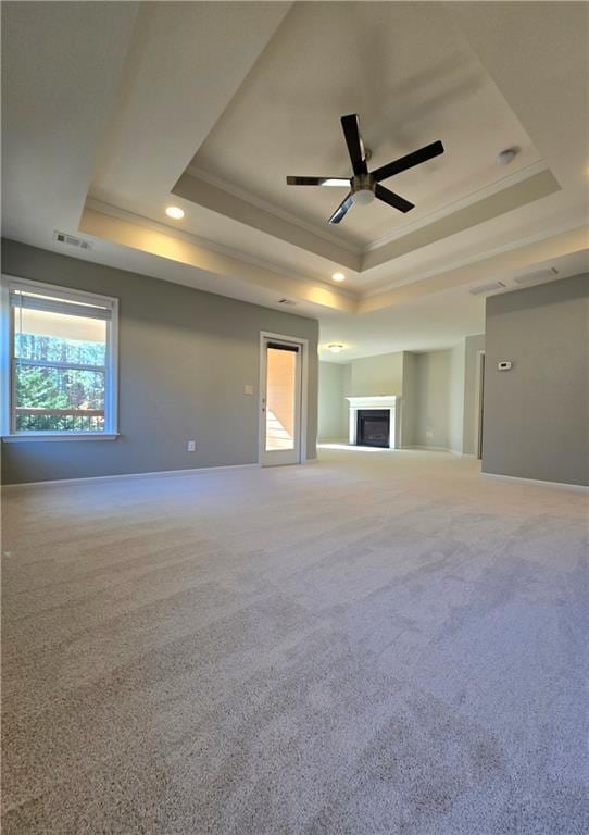 unfurnished living room with a raised ceiling, ceiling fan, carpet, and crown molding