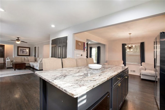 kitchen with dark wood-style flooring, decorative light fixtures, visible vents, open floor plan, and light stone countertops