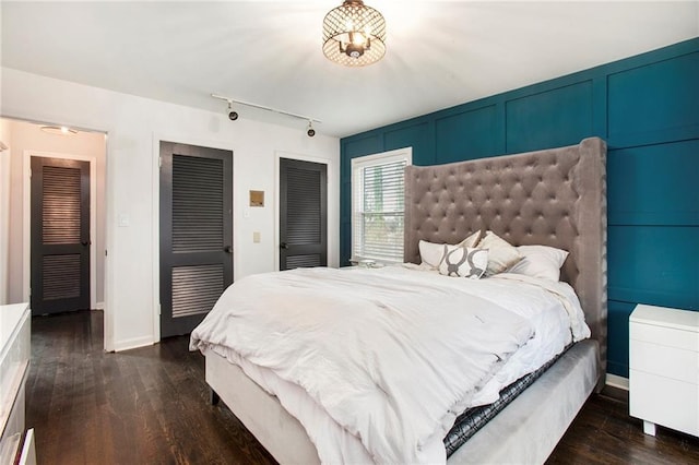 bedroom with multiple closets, track lighting, baseboards, and dark wood-style flooring