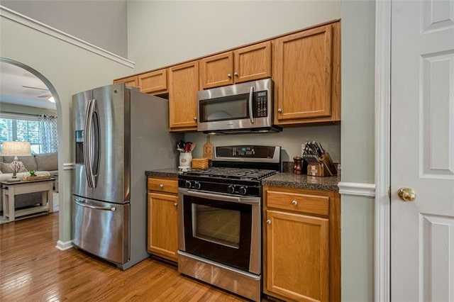 115 Oak Crest Ln, Dallas, GA 30132 - kitchen with stainless steel appliances, dark countertops, light wood-style flooring, arched walkways, and brown cabinetry