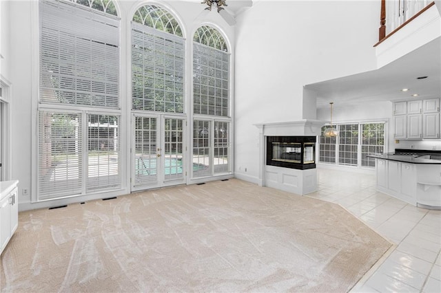 unfurnished living room featuring light colored carpet, a multi sided fireplace, a high ceiling, and ceiling fan