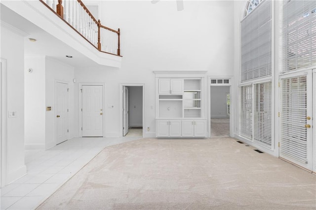 unfurnished living room featuring a towering ceiling, a healthy amount of sunlight, and light colored carpet
