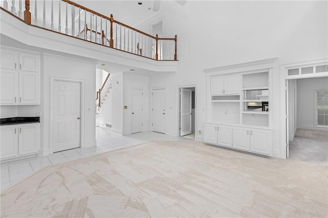 unfurnished living room with a towering ceiling, light carpet, and built in features