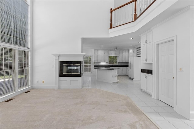 kitchen featuring white cabinetry, a kitchen island, light tile patterned floors, white fridge with ice dispenser, and a towering ceiling