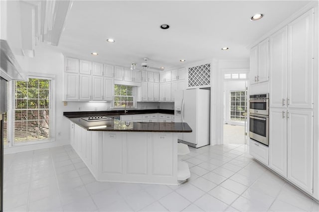 kitchen with light tile patterned floors, white refrigerator with ice dispenser, double oven, white cabinetry, and a breakfast bar area