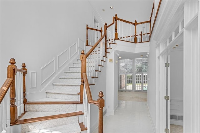 stairs with a high ceiling, ornamental molding, and tile patterned floors