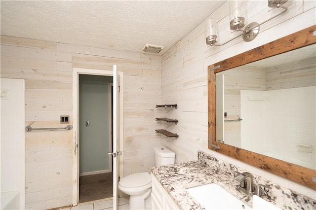 bathroom with a textured ceiling, toilet, vanity, wooden walls, and tile patterned floors