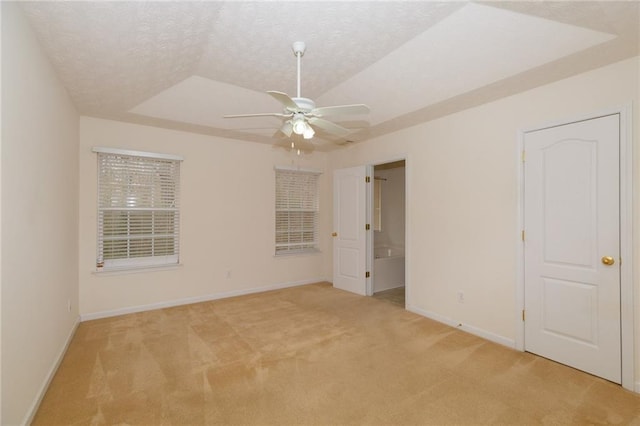 unfurnished bedroom with vaulted ceiling, light carpet, a textured ceiling, a raised ceiling, and ceiling fan