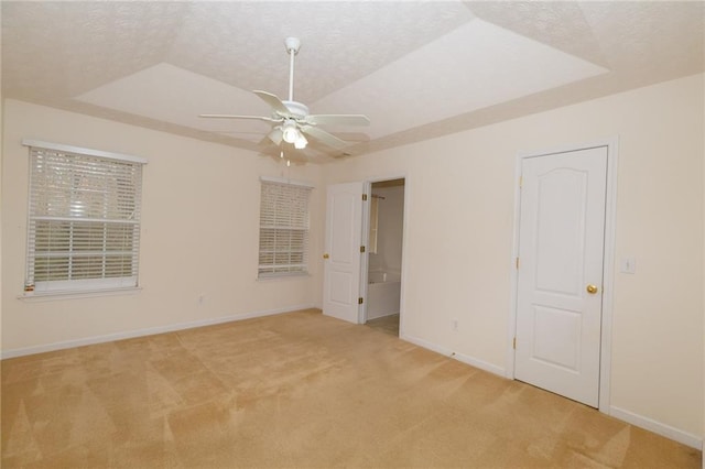 unfurnished room with a raised ceiling, ceiling fan, light carpet, and a textured ceiling