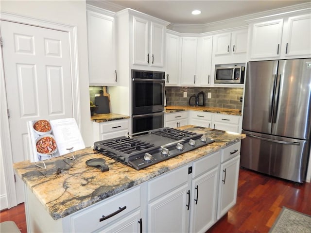 kitchen featuring white cabinets, dark wood-style floors, a kitchen island, appliances with stainless steel finishes, and light stone counters