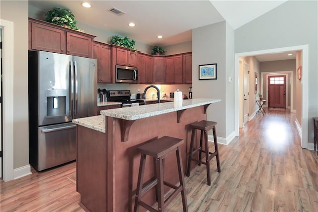 kitchen with light stone countertops, appliances with stainless steel finishes, light hardwood / wood-style flooring, and a center island with sink