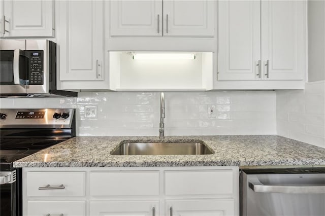 kitchen featuring decorative backsplash, appliances with stainless steel finishes, light stone countertops, a sink, and white cabinets