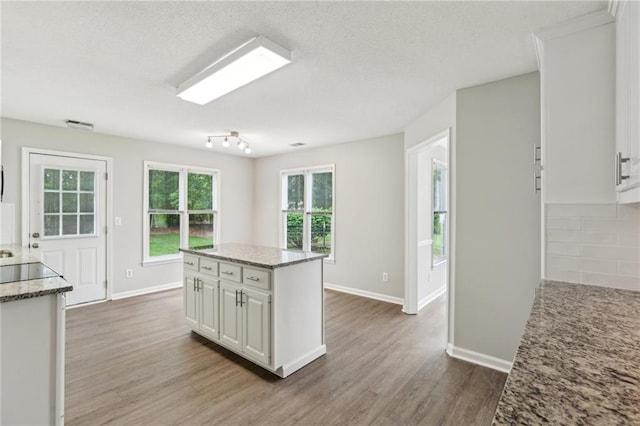 kitchen with decorative backsplash, wood finished floors, baseboards, white cabinetry, and light stone counters