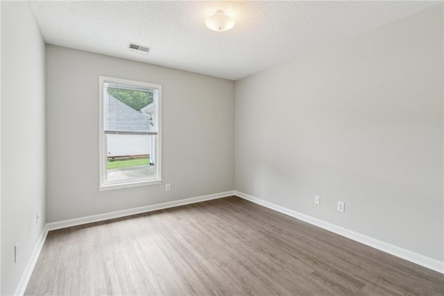 unfurnished room featuring a textured ceiling, baseboards, wood finished floors, and visible vents