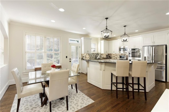 kitchen featuring a kitchen breakfast bar, stainless steel appliances, decorative light fixtures, white cabinets, and a kitchen island