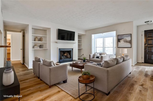 living room with a textured ceiling, light wood-type flooring, and built in features