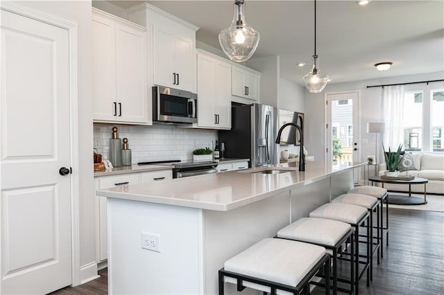 kitchen with a kitchen bar, appliances with stainless steel finishes, white cabinets, pendant lighting, and a center island with sink