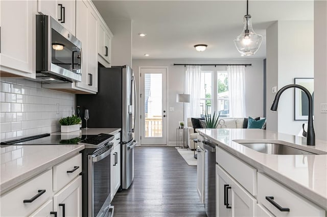 kitchen with light stone countertops, white cabinetry, sink, decorative light fixtures, and stainless steel appliances