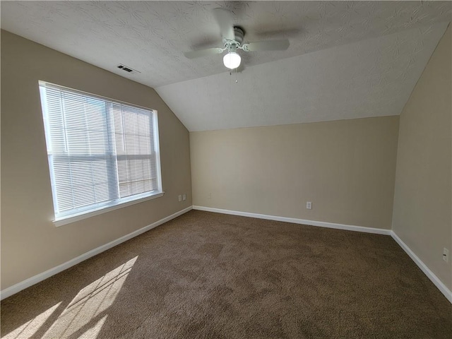 additional living space featuring dark carpet, vaulted ceiling, plenty of natural light, and ceiling fan