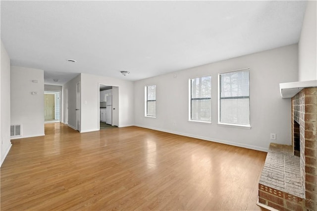 unfurnished living room featuring a brick fireplace, visible vents, baseboards, and wood finished floors