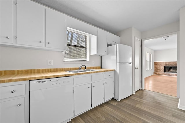 kitchen with white appliances, white cabinets, wood finished floors, a fireplace, and a sink