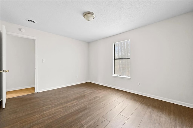 spare room with dark wood-style floors, a textured ceiling, visible vents, and baseboards