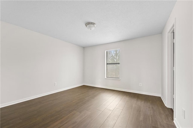 empty room with a textured ceiling, dark wood-type flooring, and baseboards