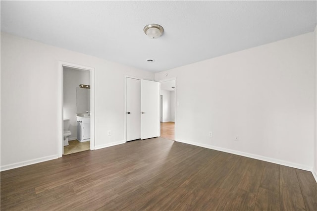 unfurnished bedroom featuring ensuite bathroom, dark wood-type flooring, and baseboards