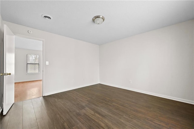 empty room with dark wood-style floors, visible vents, and baseboards