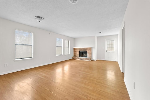 unfurnished living room with a textured ceiling, light wood-type flooring, and a brick fireplace