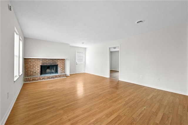 unfurnished living room featuring a brick fireplace, visible vents, light wood finished floors, and a wealth of natural light